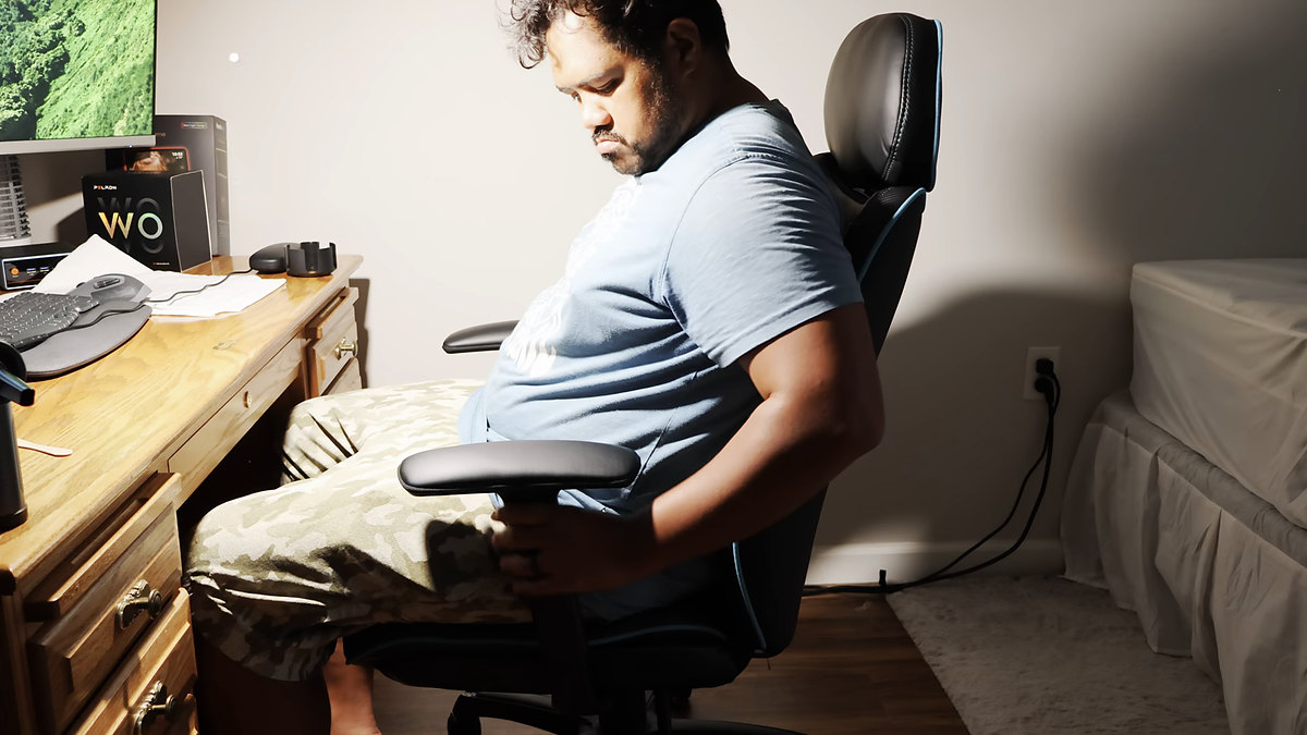Reviewer seated in black Costco DPS gaming chair with blue trim at a wooden desk — Costco compare only
